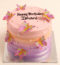 A round pink and purple ombre birthday cake decorated with edible sugar butterflies and pearls, with Happy Birthday written on top